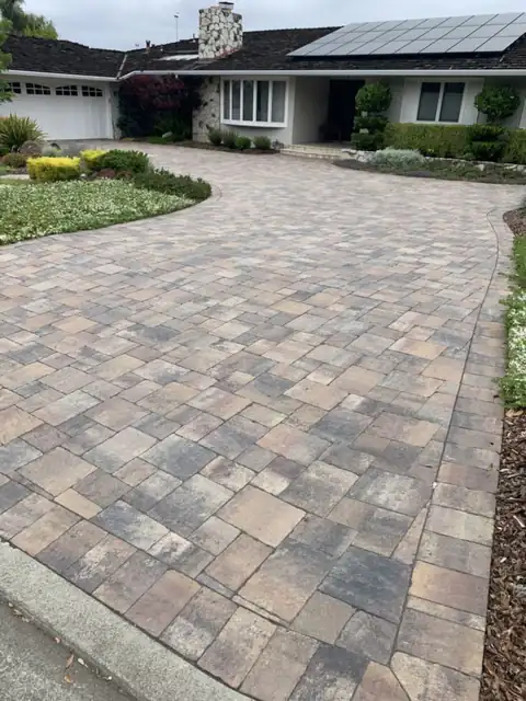 Paver driveway with blended tan and gray concrete pavers and a matching border leading to a ranch-style home